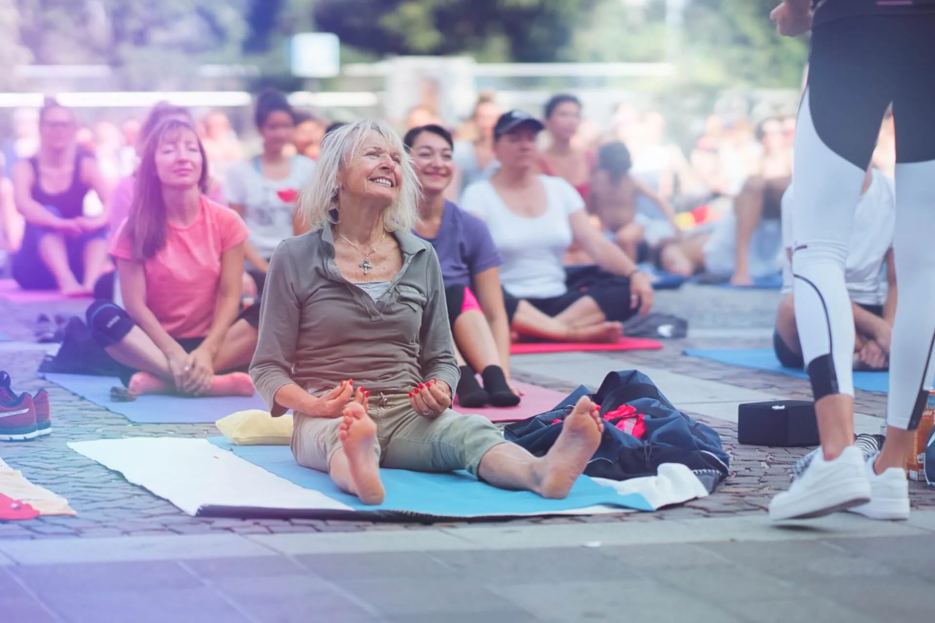 Aeltere Frau mit weissem Haar laechelt strahlend bei einem grossen Outdoor-Event, Menge im Hintergrund