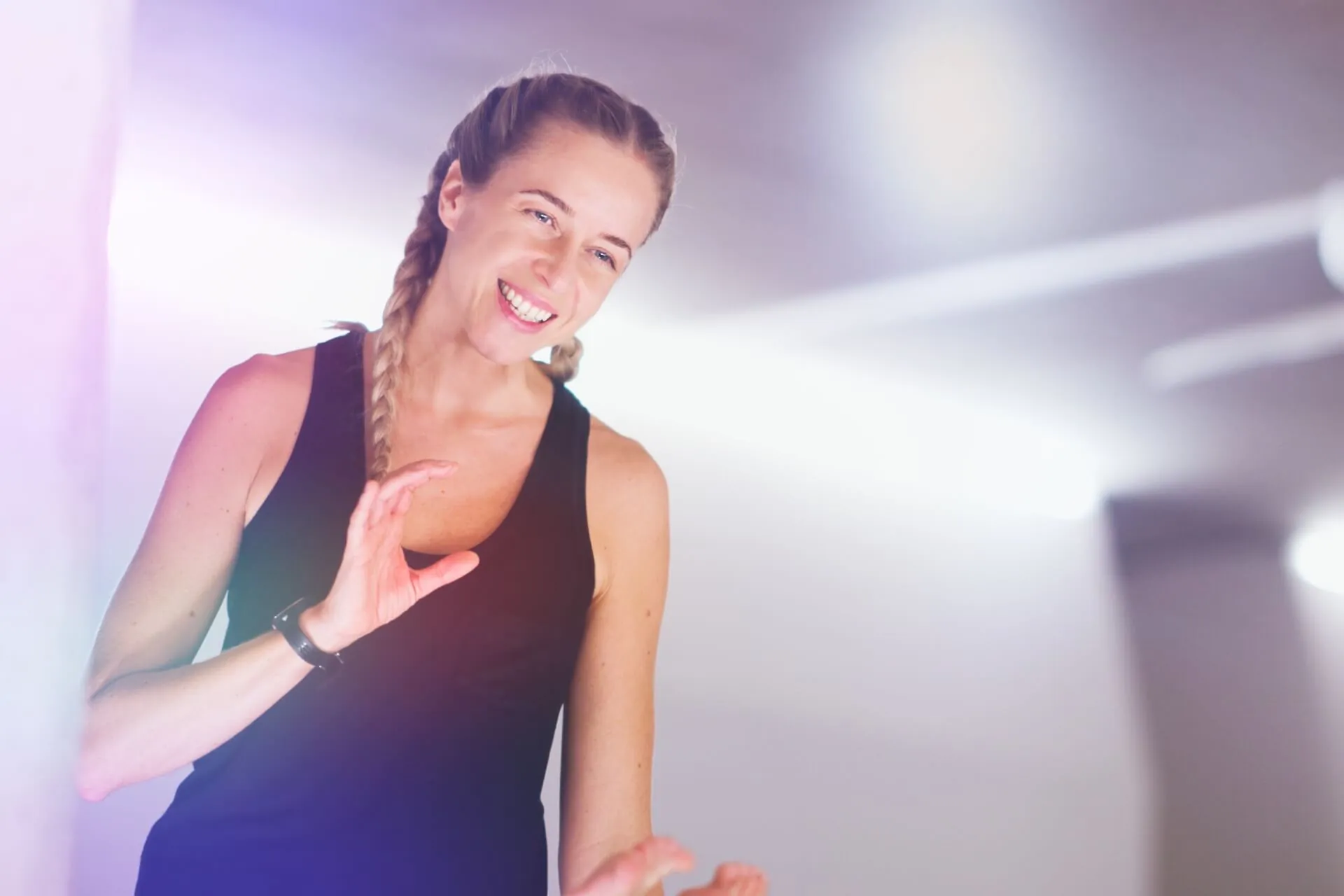 Nahaufnahme von Suzanne Freiherz, laechelnd mit geflochtenem Haar, schwarzes Top, warmes Studiolicht