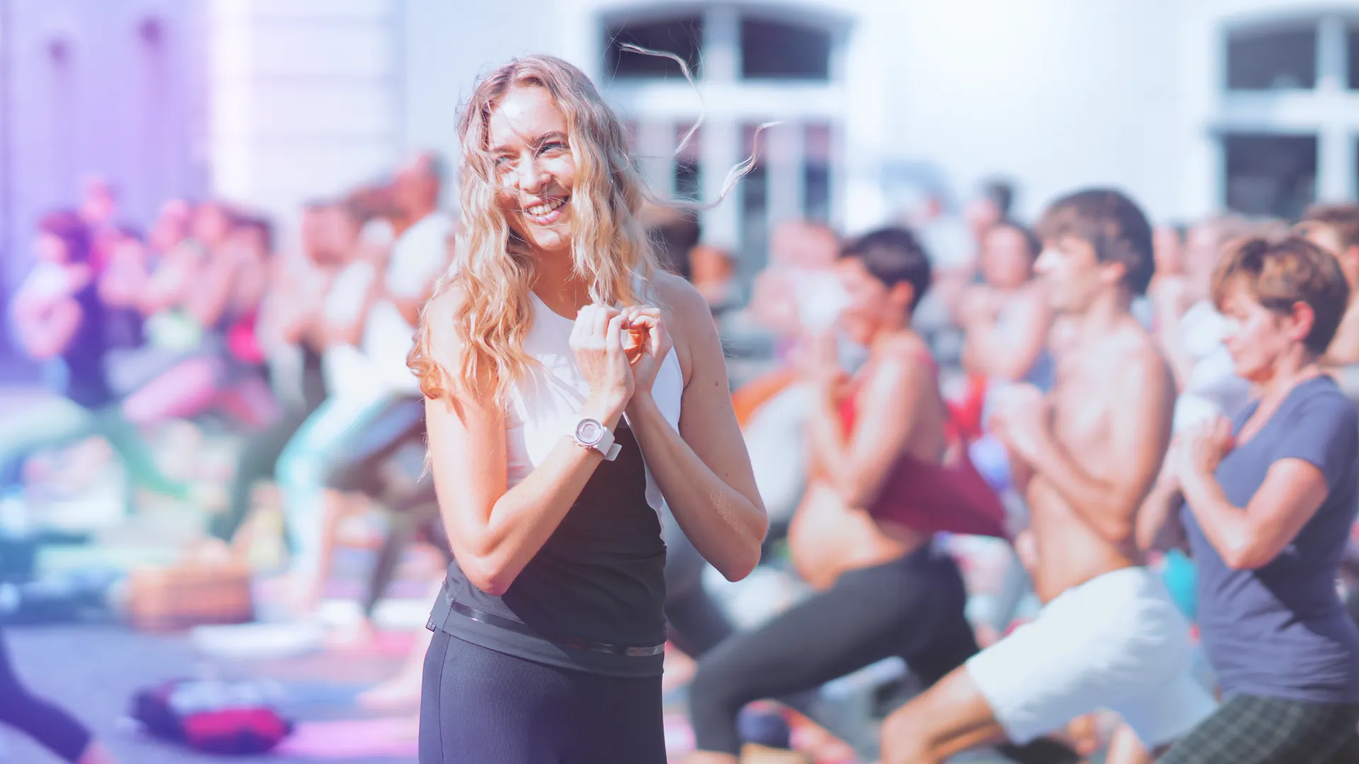Suzanne laechelnd, Haende nahe der Brust, Menge hinter ihr